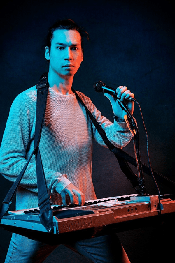 Huge Davies on stage playing a keyboard and holding a microphone